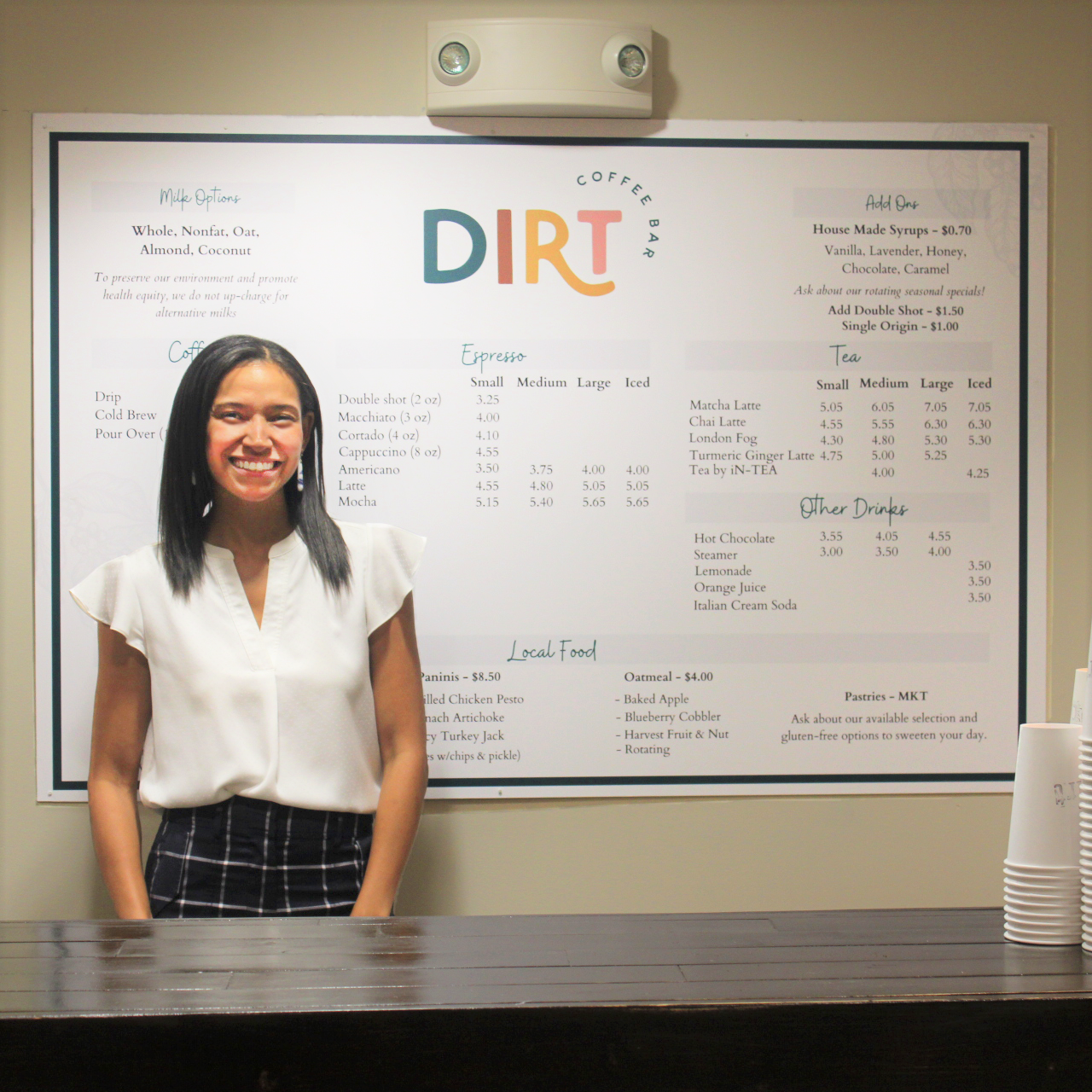 Catharina Hughey, Executive Director of Dirt Coffee in front of the Dirt Coffee menu