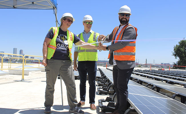 three people cut a ribbon on a rooftop with solar panels